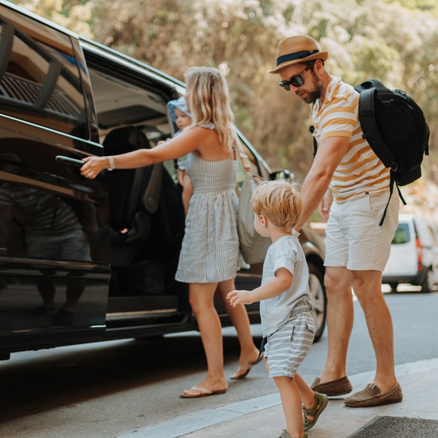 Parents with toddlers boarding car for airport transfer or holiday trip